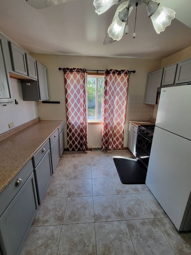 kitchen featuring ceiling fan, light tile patterned floors, tasteful backsplash, gray cabinets, and white fridge