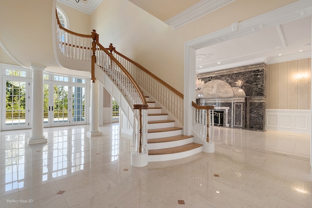 stairs with a towering ceiling, ornamental molding, a premium fireplace, and ornate columns