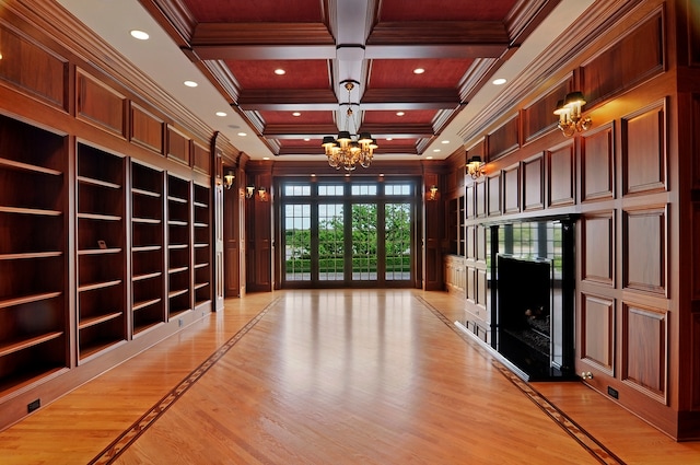 interior space featuring light hardwood / wood-style floors, coffered ceiling, a fireplace, an inviting chandelier, and ornamental molding