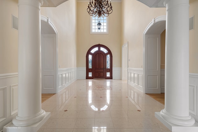 entrance foyer with an inviting chandelier, a towering ceiling, decorative columns, and crown molding