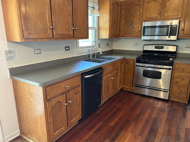 kitchen featuring appliances with stainless steel finishes, sink, decorative light fixtures, and dark hardwood / wood-style flooring