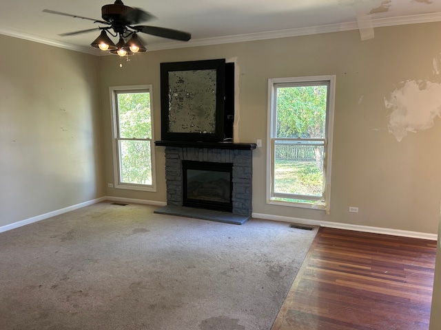 unfurnished living room featuring ceiling fan, a stone fireplace, ornamental molding, and wood-type flooring