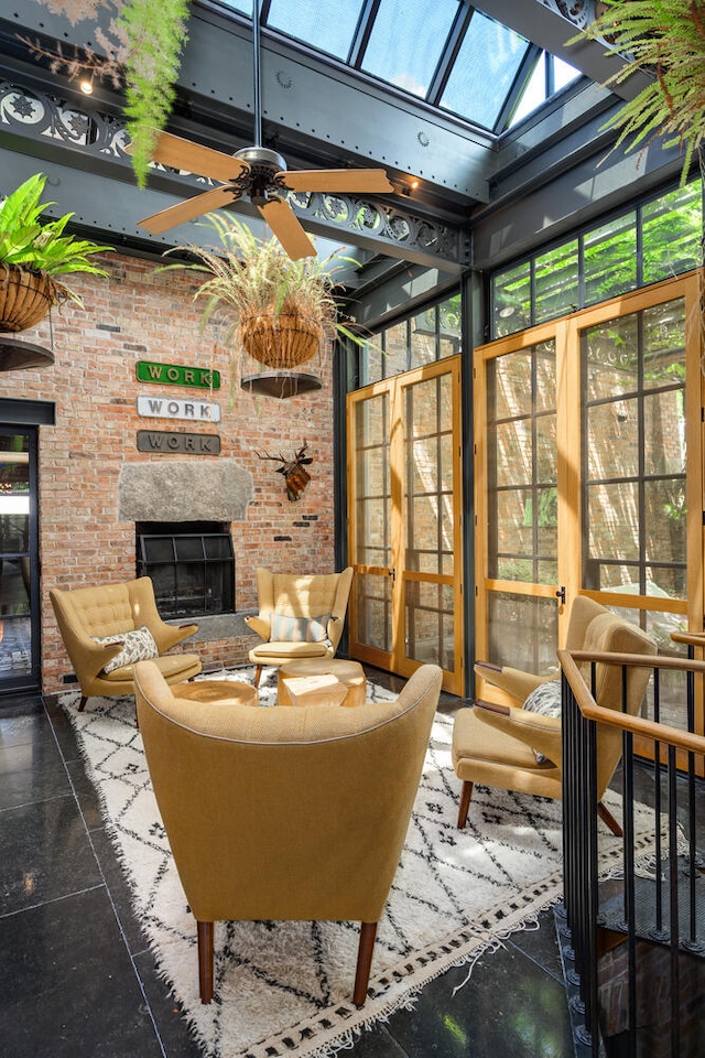 sunroom with plenty of natural light, lofted ceiling with skylight, ceiling fan, and a brick fireplace