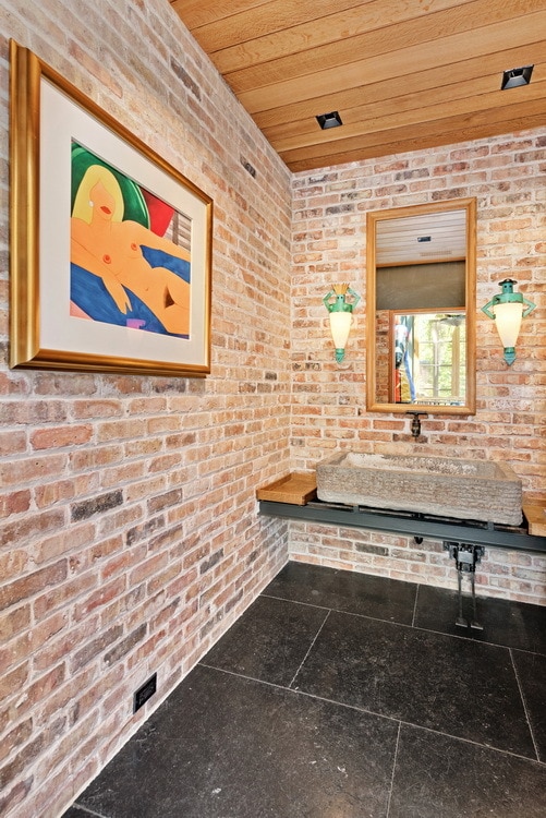 bathroom with wood ceiling and brick wall