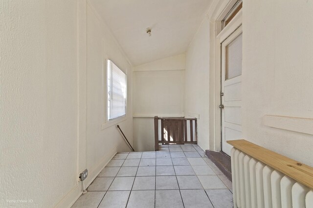 corridor featuring radiator, lofted ceiling, and light tile patterned floors