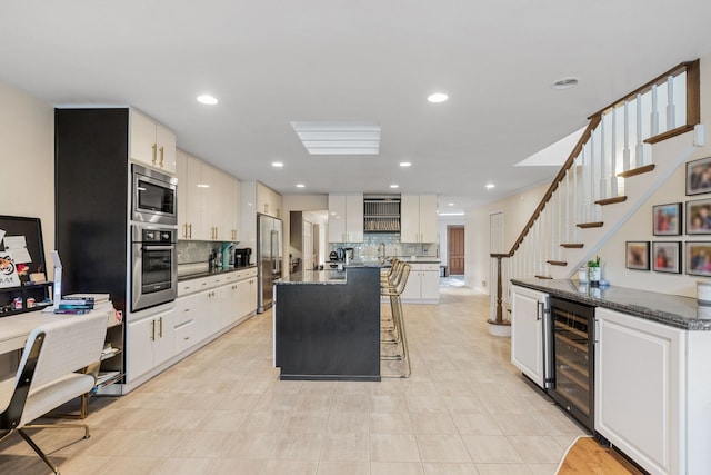 kitchen with appliances with stainless steel finishes, white cabinetry, tasteful backsplash, a center island, and beverage cooler