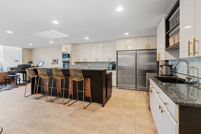 kitchen with dark stone counters, a center island, built in appliances, sink, and white cabinets