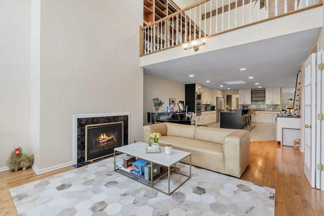 living room with a towering ceiling, a fireplace, and light wood-type flooring