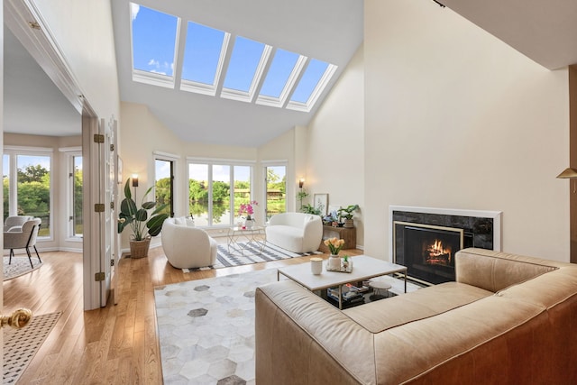 living room with a high end fireplace, light hardwood / wood-style flooring, a skylight, and high vaulted ceiling