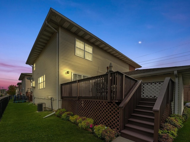 back house at dusk featuring a yard, central air condition unit, and a wooden deck