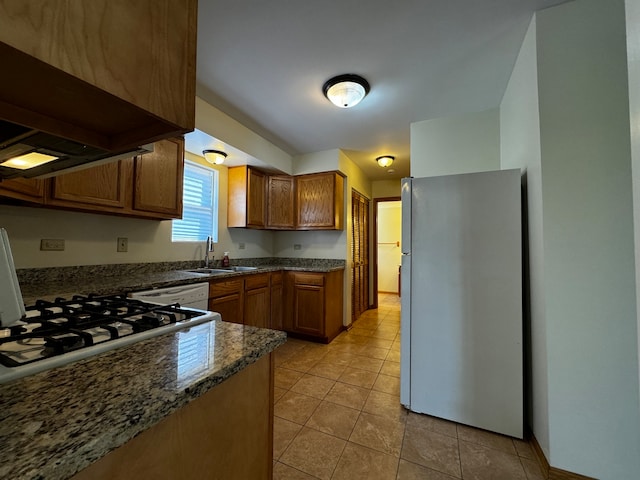 kitchen with custom range hood, light tile patterned floors, dark stone counters, refrigerator, and sink