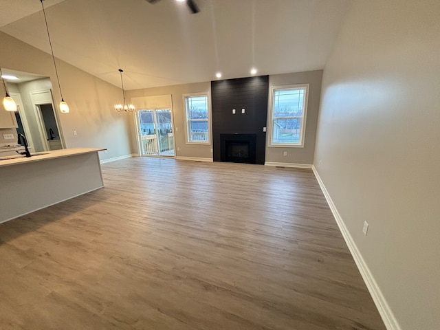 unfurnished living room with hardwood / wood-style floors, a notable chandelier, a fireplace, and vaulted ceiling