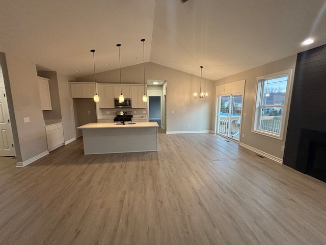 kitchen featuring pendant lighting, light hardwood / wood-style floors, white cabinetry, and an island with sink