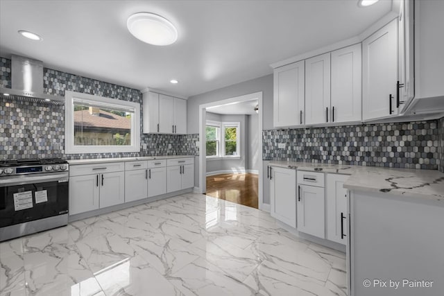 kitchen with light stone counters, tasteful backsplash, white cabinets, stainless steel stove, and wall chimney exhaust hood