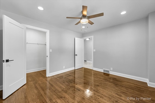 unfurnished bedroom featuring dark hardwood / wood-style floors, ceiling fan, a walk in closet, and a closet