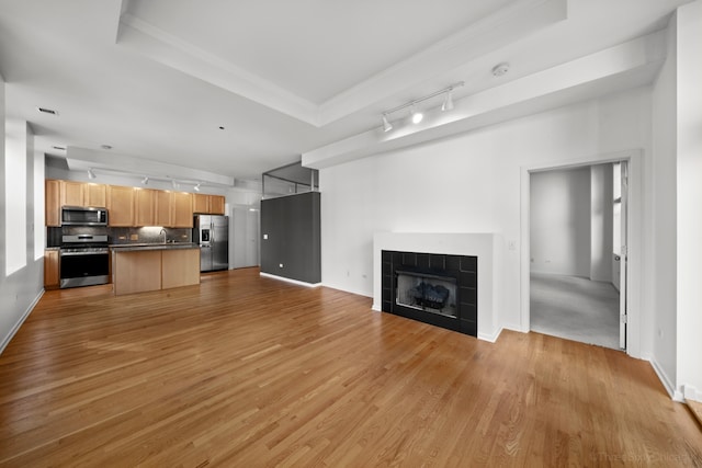 unfurnished living room with light wood-type flooring, a tray ceiling, a tiled fireplace, and track lighting