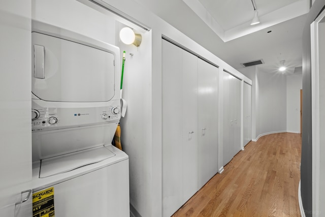 clothes washing area featuring light wood-type flooring, stacked washer and clothes dryer, and rail lighting