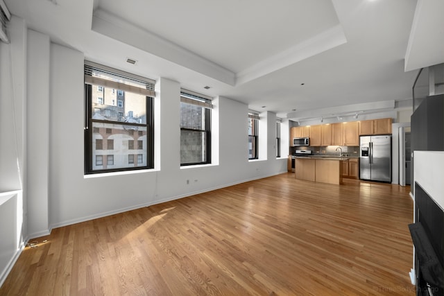 unfurnished living room featuring sink, a raised ceiling, and light hardwood / wood-style floors