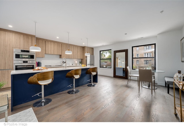 kitchen with wood-type flooring, appliances with stainless steel finishes, decorative light fixtures, and a breakfast bar area