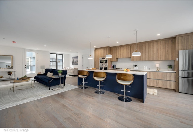 kitchen with hanging light fixtures, light hardwood / wood-style floors, a breakfast bar area, stainless steel appliances, and a kitchen island with sink