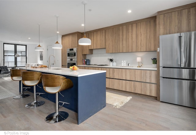 kitchen with pendant lighting, an island with sink, sink, appliances with stainless steel finishes, and light wood-type flooring