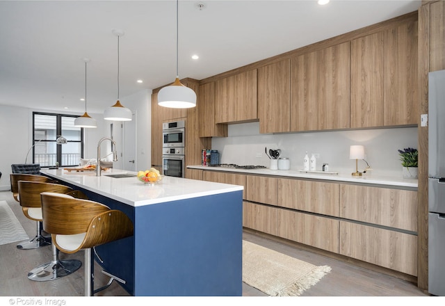 kitchen featuring pendant lighting, light wood-type flooring, a kitchen bar, a kitchen island with sink, and sink