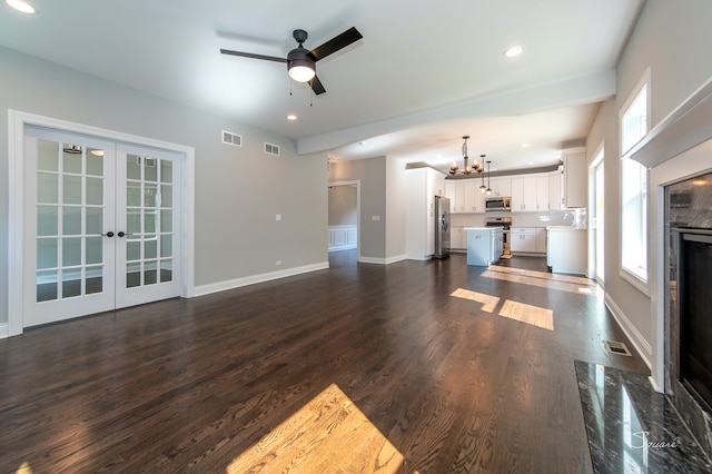 unfurnished living room featuring ceiling fan with notable chandelier, a fireplace, dark wood-type flooring, and french doors