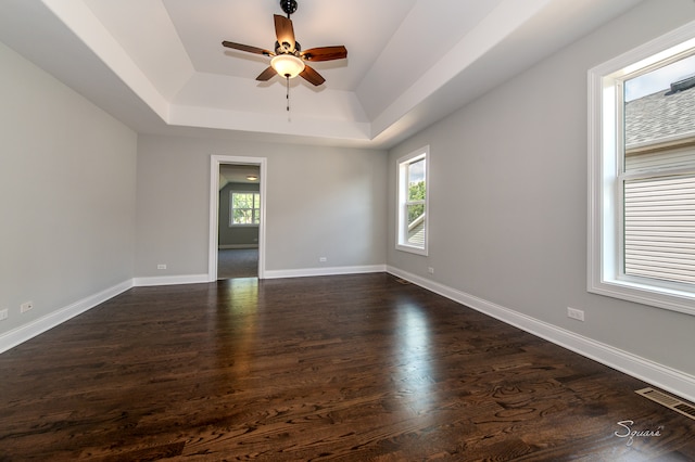 empty room with ceiling fan, a tray ceiling, and dark hardwood / wood-style floors