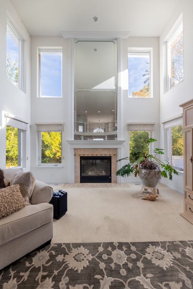 living room with a tile fireplace, carpet, a towering ceiling, and plenty of natural light