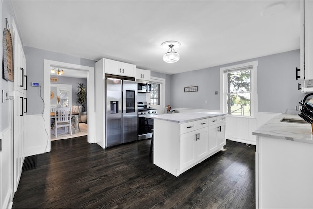 kitchen with white cabinetry, a kitchen island, light stone countertops, stainless steel appliances, and dark hardwood / wood-style floors