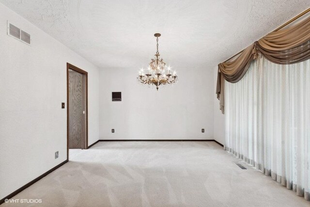 carpeted empty room featuring a notable chandelier and a textured ceiling