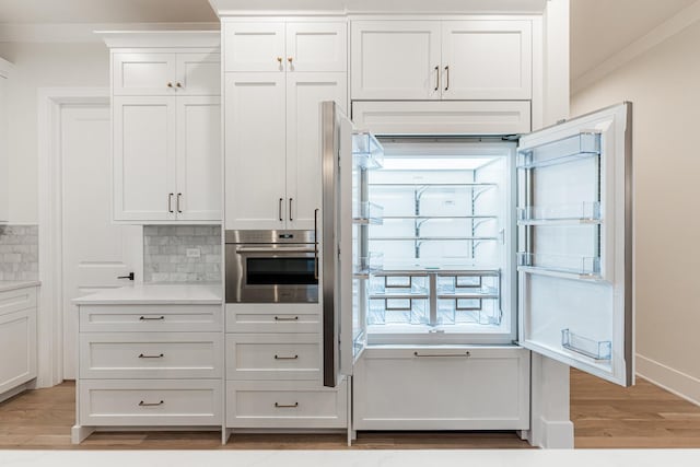 kitchen featuring tasteful backsplash, white cabinets, oven, light hardwood / wood-style floors, and crown molding