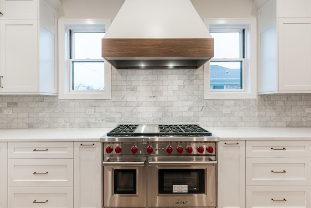 kitchen featuring custom exhaust hood, double oven range, tasteful backsplash, and white cabinets