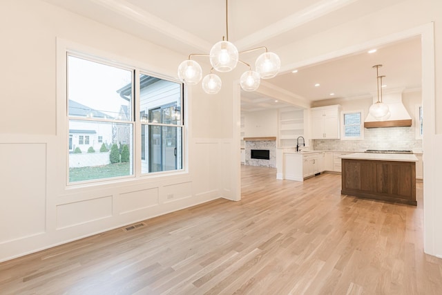 kitchen featuring gas stovetop, white cabinetry, decorative light fixtures, a center island, and light wood-type flooring