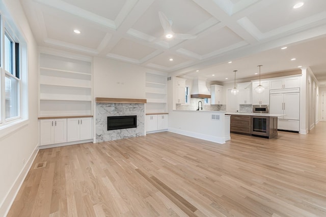 unfurnished living room featuring wine cooler, sink, coffered ceiling, and light hardwood / wood-style floors