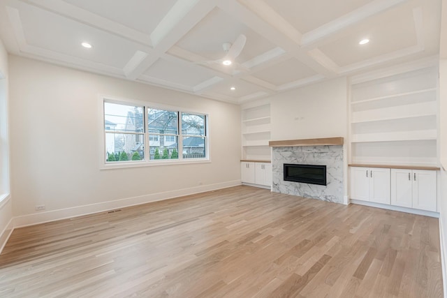 unfurnished living room featuring coffered ceiling, built in features, beamed ceiling, a fireplace, and light hardwood / wood-style floors