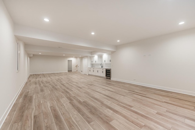 unfurnished living room featuring beverage cooler, light hardwood / wood-style flooring, and wet bar