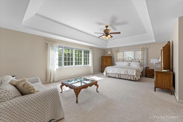 bedroom with multiple windows, light carpet, a tray ceiling, and ceiling fan