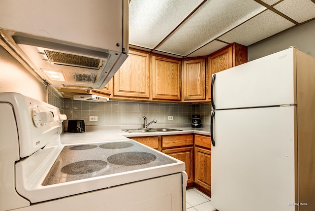 kitchen with light countertops, tasteful backsplash, white appliances, a sink, and brown cabinets