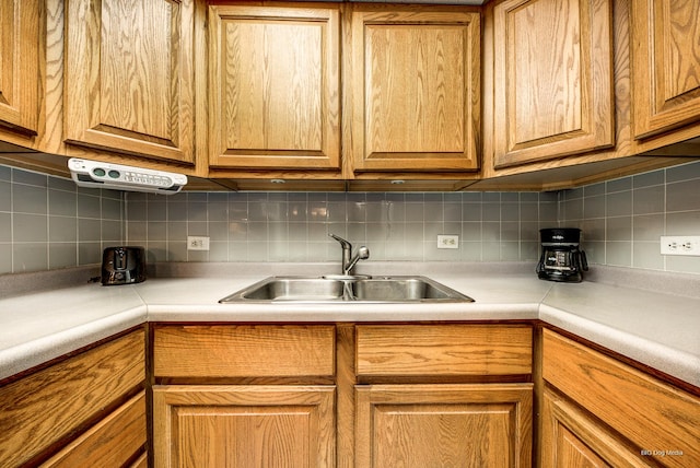 kitchen featuring light countertops, a sink, tasteful backsplash, and brown cabinetry