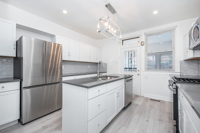 kitchen featuring white cabinets, stainless steel appliances, hanging light fixtures, and light hardwood / wood-style flooring