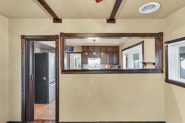 kitchen featuring beamed ceiling, hanging light fixtures, light tile patterned floors, and stainless steel refrigerator