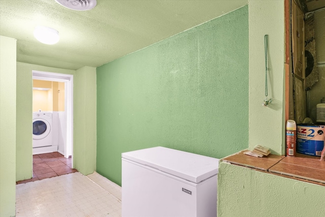 clothes washing area with a textured ceiling, light tile patterned floors, and washer / clothes dryer