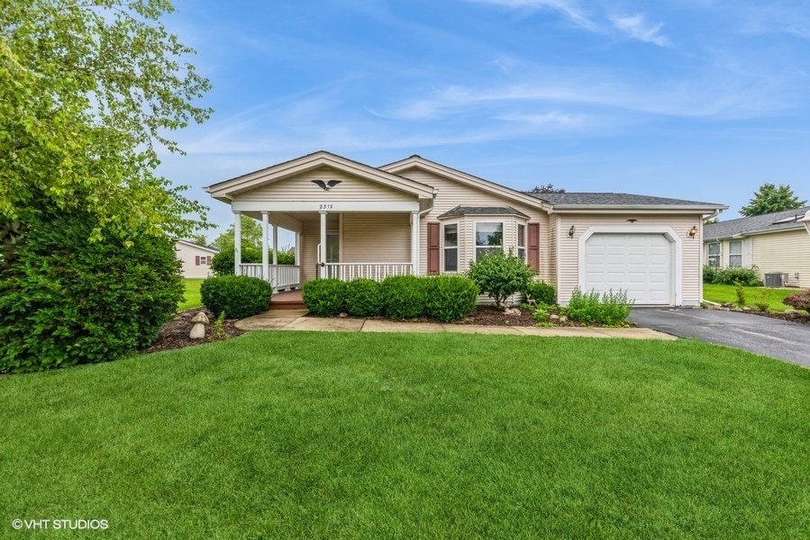 ranch-style home with a porch, a garage, central AC unit, and a front lawn