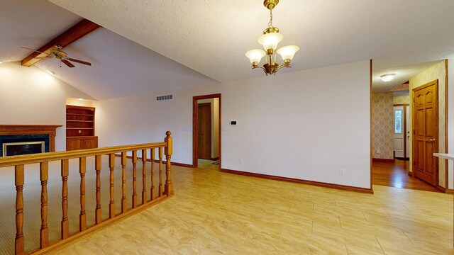 empty room with lofted ceiling with beams, ceiling fan with notable chandelier, light hardwood / wood-style flooring, a premium fireplace, and a textured ceiling