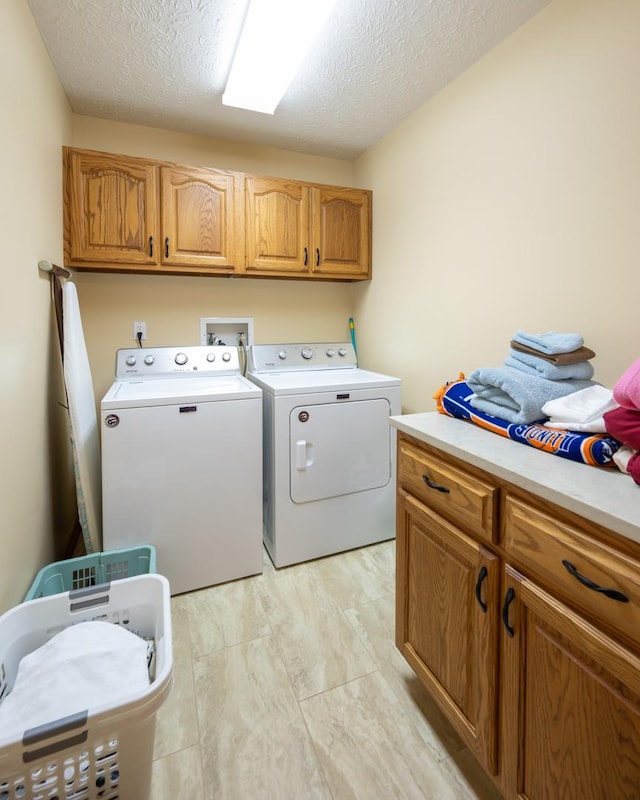 clothes washing area with cabinets, a textured ceiling, and washing machine and clothes dryer