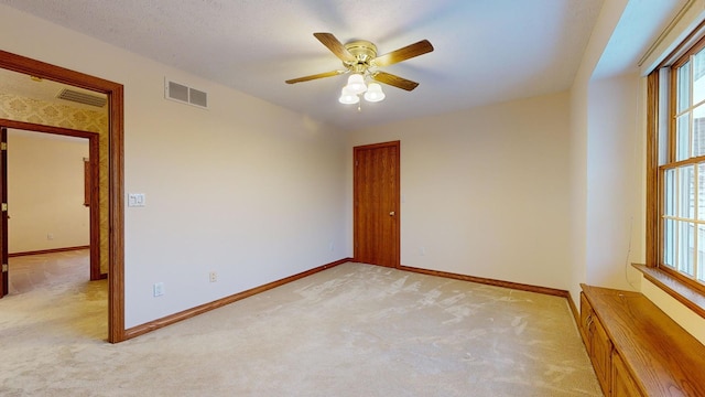 empty room featuring a textured ceiling, light colored carpet, and ceiling fan