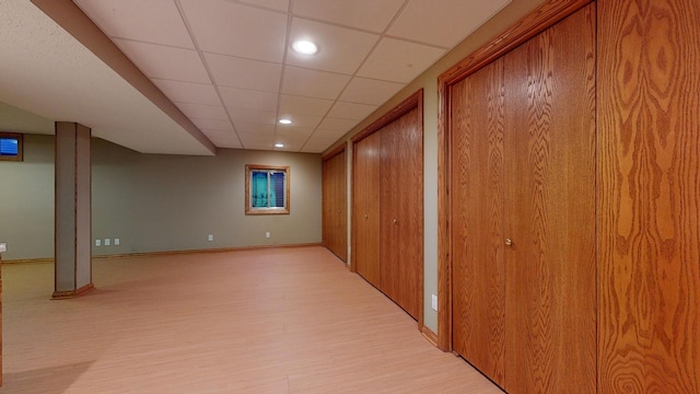 basement featuring a paneled ceiling and light hardwood / wood-style flooring