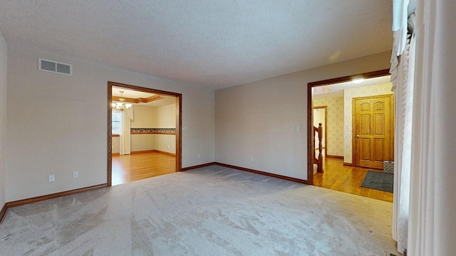 empty room with a textured ceiling, light hardwood / wood-style flooring, and a notable chandelier