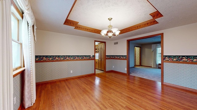 empty room with a wealth of natural light, hardwood / wood-style floors, a textured ceiling, and an inviting chandelier